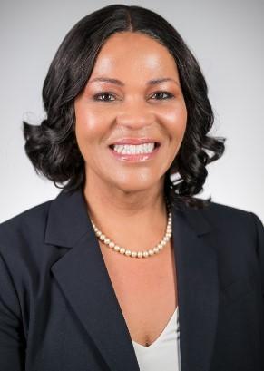 A Black woman in a suit and pearls smiles for a headshot