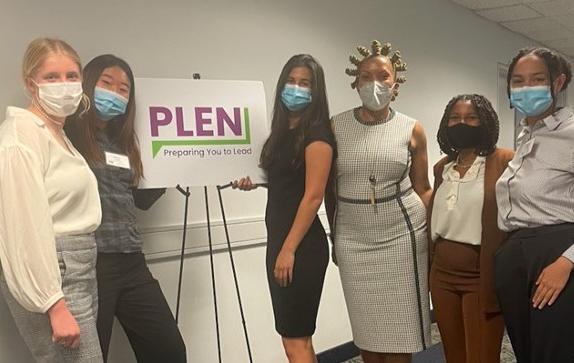 A group of women wearing medical masks stand in front a sign