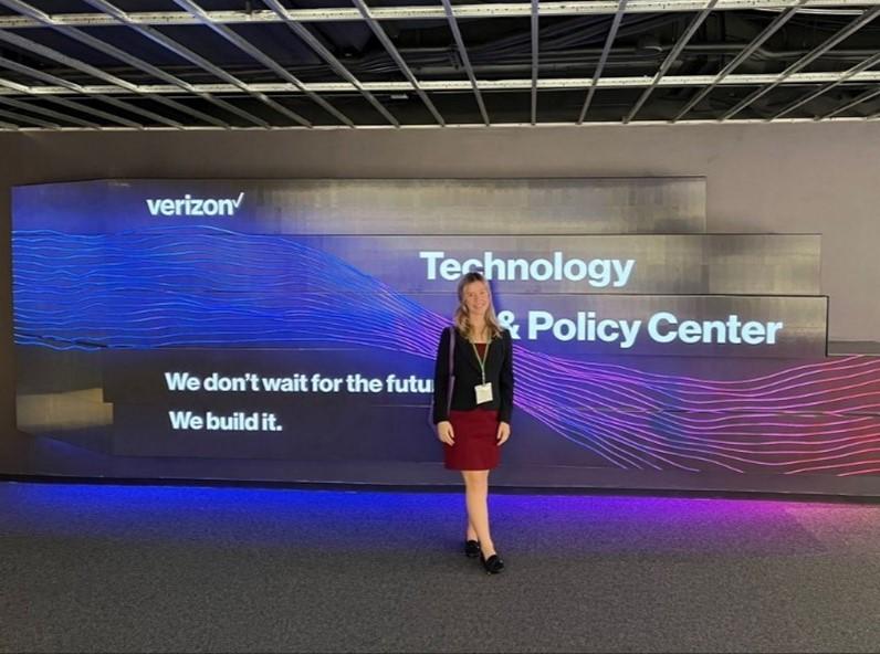 woman stands in front of a screen that says "Technology & Policy Center"