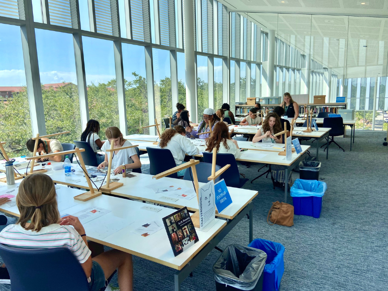 a group of students sit at tables in a sunny glass room