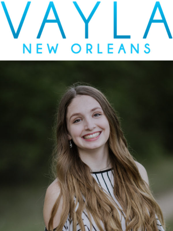 White woman stands in front of a blurred nature background under the Vayla New Orleans logo