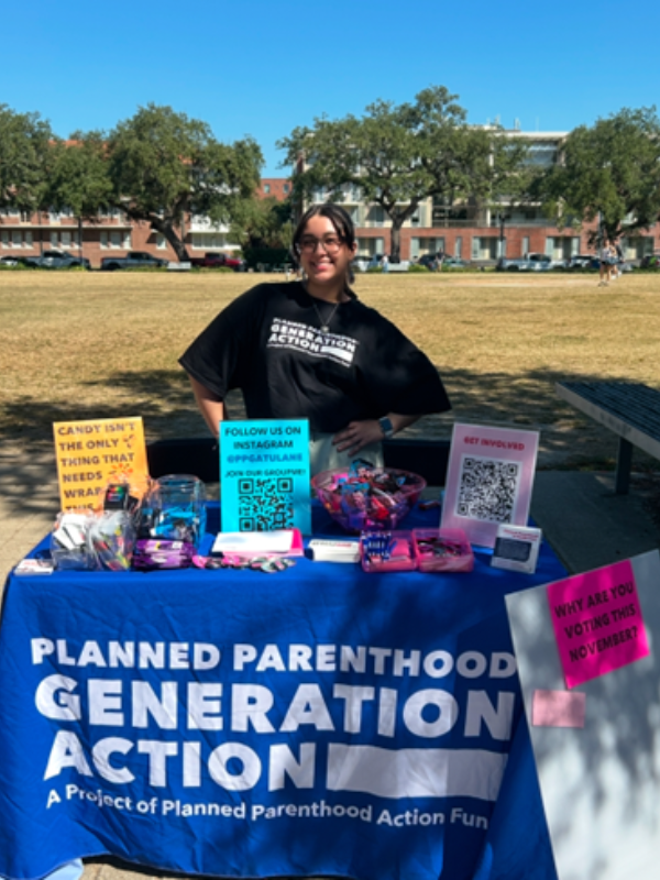 A Woman stands behind a table with a sign that says Planned Parenthood Generation Action