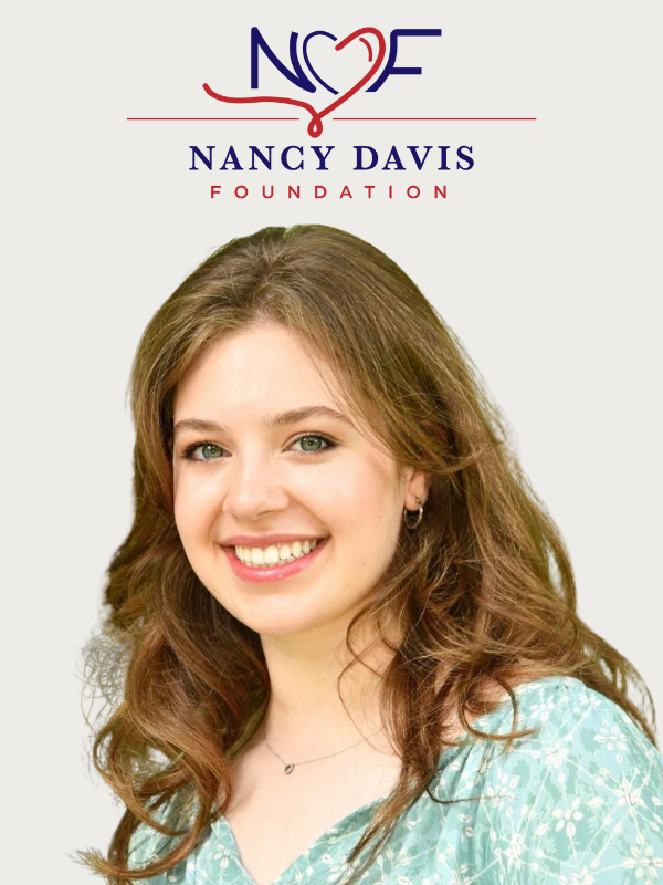 A White woman stands under the Nancy Davis Foundation Logo with a gray background