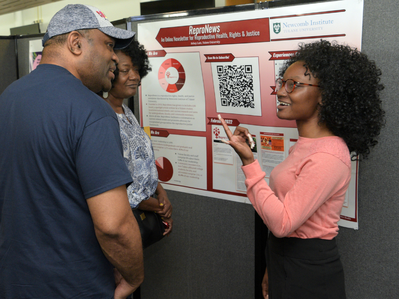 Student stands in front of a scientific poster while talking two people