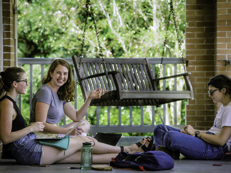three students sit on a porch talking together