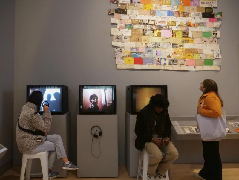 Students in a museum explore the exhbit, including computers and a collage.