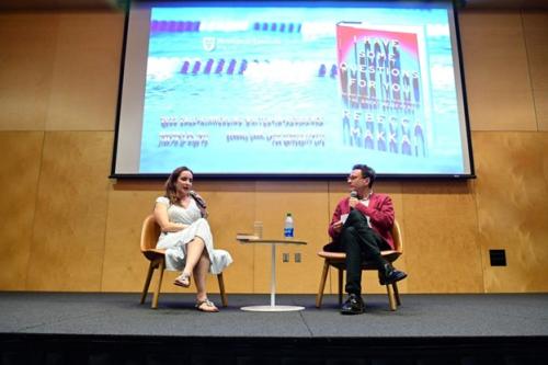 Two women sit on a stage in front of a projector screen