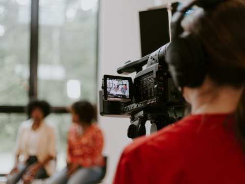 Woman in foreground recording with a video camera in the distance two woman talk to each other