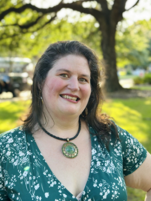 A white woman in front of a tree wearing green and smiling