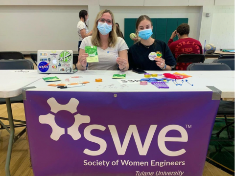 Students table at student organizations info session. They sit behind a desk with a purple table cloth.