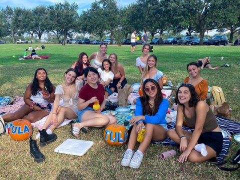 A group of students sits outside on a lawn at a park with decorated pumpkins