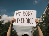 person holds up paper sign reading "My Body, My Choice." They are outside.