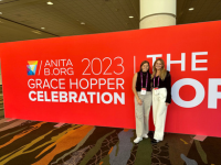 Abby Scarry and Sydney Feldman posing in front of the Grace Hopper Celebration banner