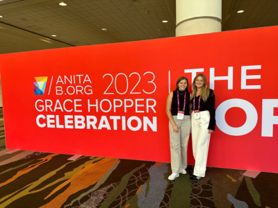 Abby Scarry ad Sydney Feldman posing in front of the Grace Hopper Celebration banner