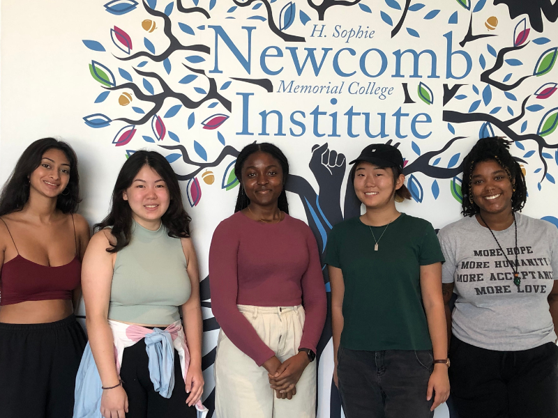 Student Interns working in the Lab stand in front of colorful mural 