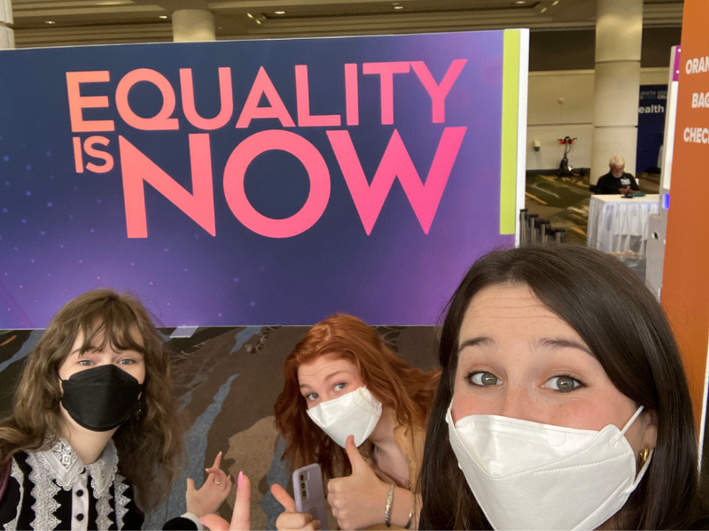 Three students stand in front of a banner reading "Equilty Now" at Tech Conference